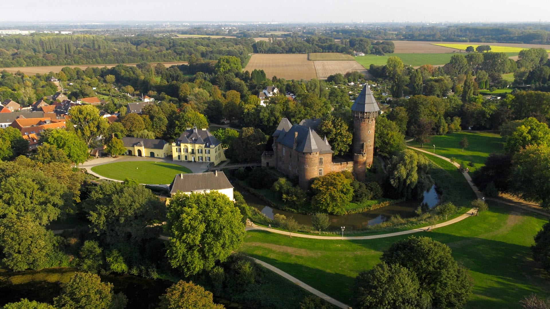 Luftaufnahme einer historischen Burg mit rotem Backstein, umgeben von grünen Bäumen und Landschaft.
