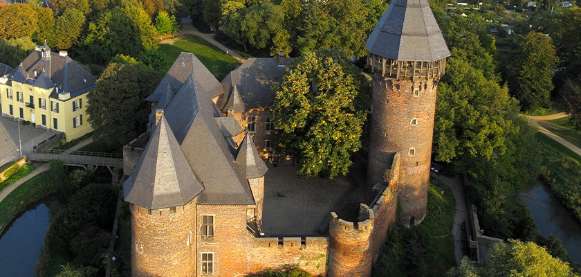 Luftaufnahme einer mittelalterlichen Backsteinburg mit runden Türmen, umgeben von Bäumen.
