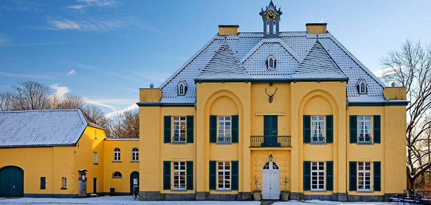 Gelbes Schloss mit Schneedecke, symmetrische Architektur, grünen Fensterläden, Uhrturm.