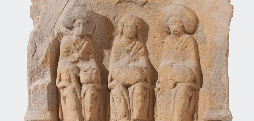 Drei sitzende Figuren auf altertümlichem Relief, ernst, mit detaillierten Gewändern, beige Stein.