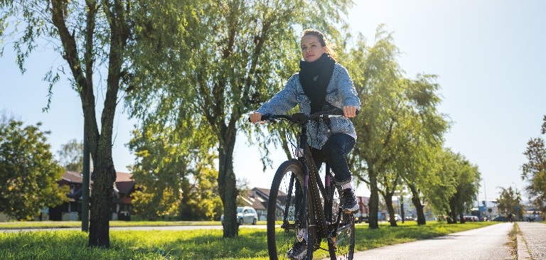 Eine Frau fährt mit dem Fahrrad außerhalb des Stadtzentrums und genießt eine erholsame Flucht aus dem Stadtleben, um ihre Gesundheit und ihr Wohlbefinden zu verbessern.
