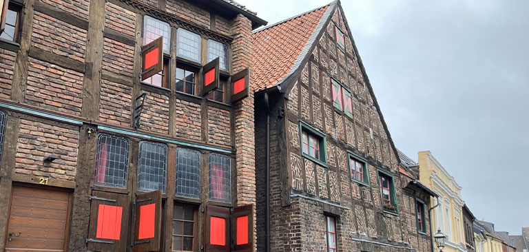 Historisches Fachwerkhaus mit roten Fensterläden und gemustertem Backsteinmuster. Bewölkter Himmel.