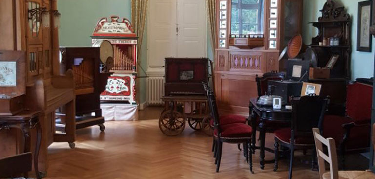 Ein Zimmer mit antiken Musikinstrumenten, darunter Drehorgeln und ein Holzklavier.