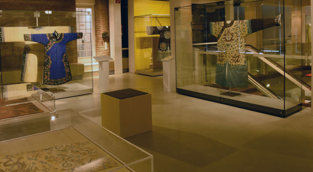 Ausstellung mit traditionellen, farbenfrohen Roben in Vitrinen, beleuchtet mit warmem Licht.