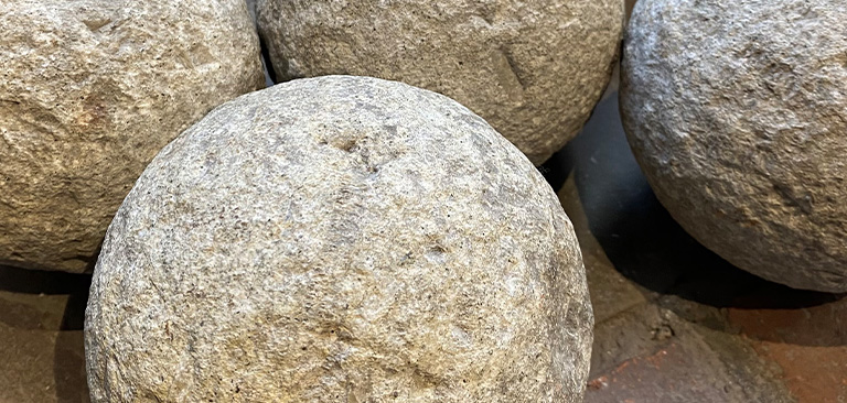 Steinkugeln aus grauem Gestein mit texturierter Oberfläche, gruppiert auf einem dunklen Untergrund.