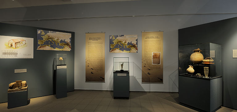 Ein Museumsaal mit antiken Artefakten und Informationstafeln in neutralen Farben.
