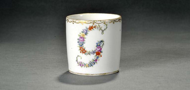 Weiße Tasse mit Blumenschrift "G", goldenen Rändern, elegant und schlicht.