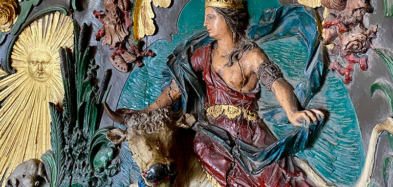 Skulptur: Frau mit Krone auf Stier, bunte Kleidung, religiöse Symbolik, goldene Verzierungen.