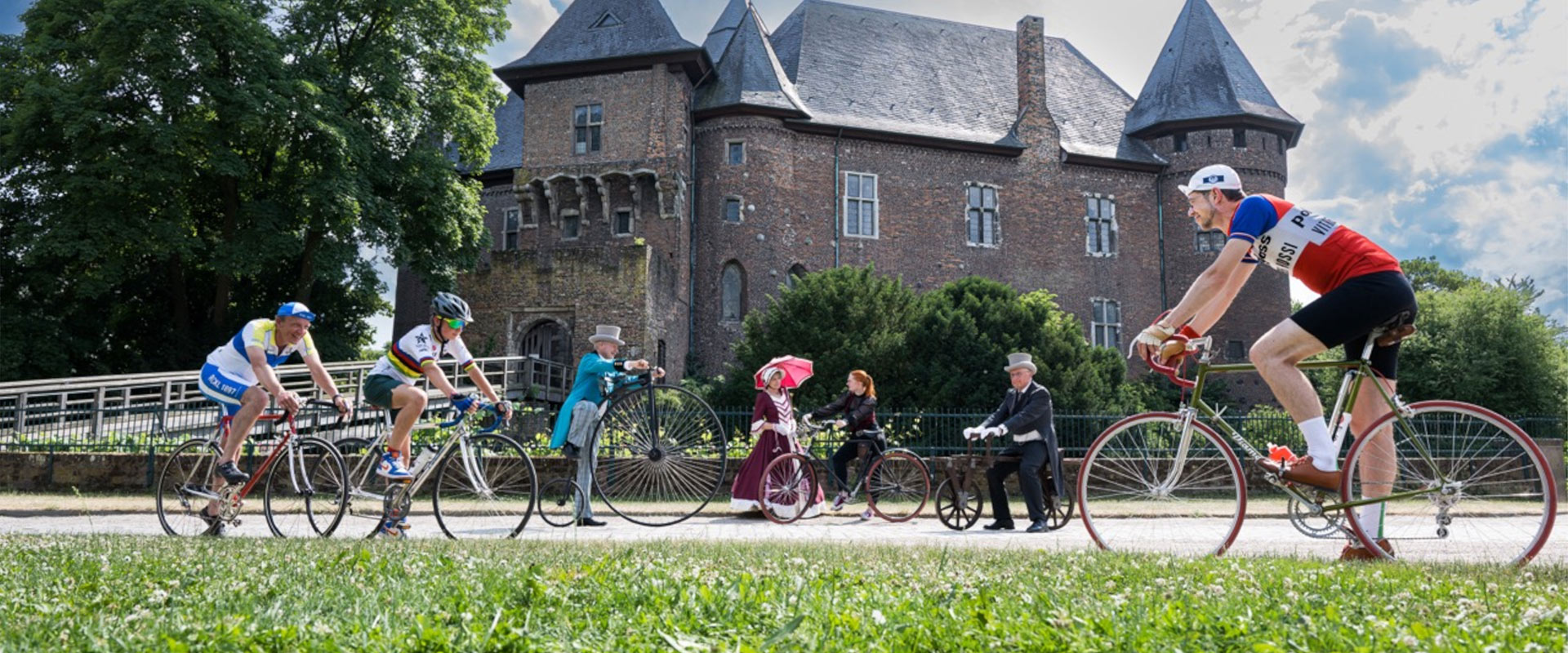 Menschen in historischer Fahrradkleidung vor einem alten Schloss, lächelnd und posierend.