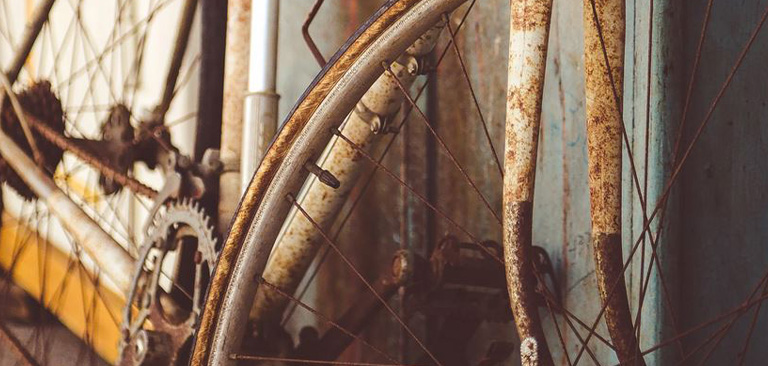 Rostiges Fahrrad mit abgenutztem Zahnkranz und Kette, vor blauer Metallwand.
