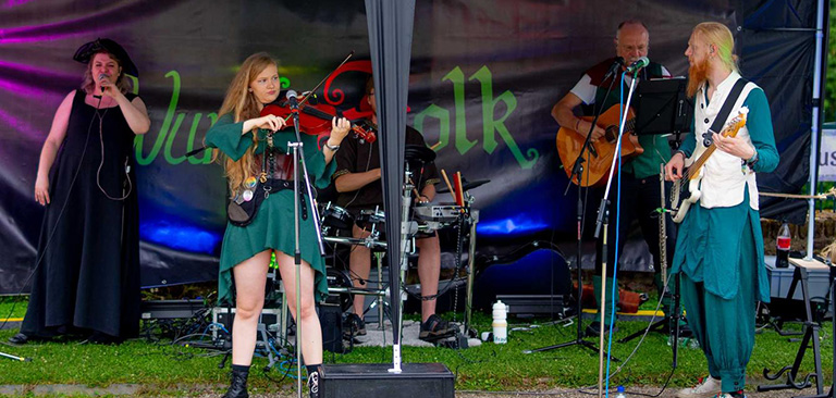 Eine Folkband spielt draußen; eine Frau in Grün spielt Geige, andere singen und begleiten.