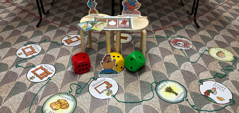 Ein Lernspiel mit Karten, farbigen Würfeln und kreisförmigen Spielfeldern auf gemustertem Teppich.